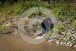 Black plastic drainage culvert pipe releasing water into a stream, environmental safety issue