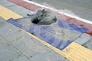 A black plastic garbage bag on a blue plastic on the floor in the street with a cement scrap