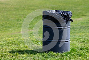 Black plastic garbage bin on green grass in park. Selective focus