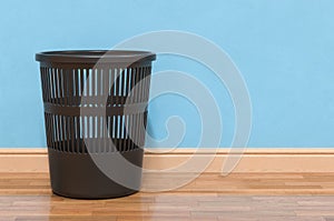 Black plastic garbage bin in room near wall. 3D rendering