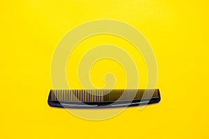 Black plastic hair comb on yellow background. Top view. Copy, empty space for text