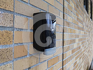 A black plastic hand sanitizer dispenser attached to a red brick wall on the outside of a building