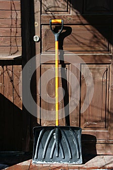 Black plastic snow shovel with orange handle at the wooden door