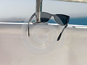 Black plastic sunglasses hang on an iron railing on a yacht against the backdrop of the sea