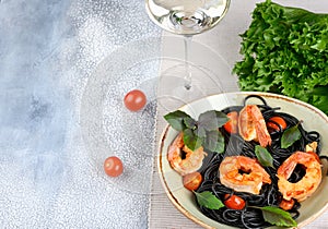 Black plate with black Nero spaghetti with langoustines, cherry and garlic, green lettuce leaves and cherry tomatoes