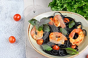 Black plate with black Nero spaghetti with langoustines, cherry and garlic, green lettuce leaves and cherry tomatoes
