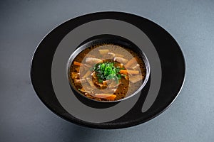 black plate with brown soup pottage with mushroom, carrot, vegetables, dill