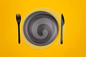 Black plate, fork, knife on yellow background.