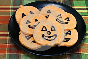 A black plate of orange pumpkin cookies with faces.  Macro, top view