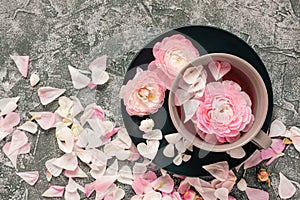 Black plate with ranunculus flowers and petals on grey concrete background. Top view