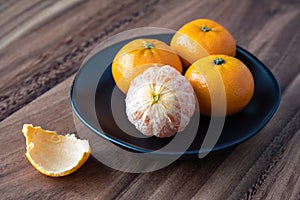 Black plate of satsuma oranges on a rustic wood table