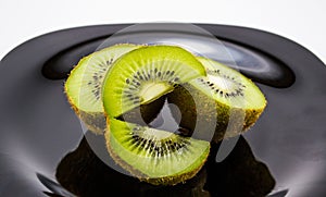 Black plate with several sliced kiwis against a dark background