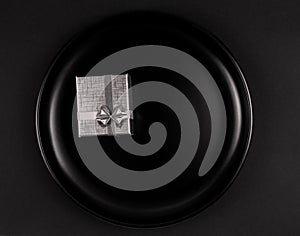 Black plate with silver gift box on black background flatlay with copy space
