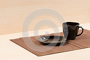 Black plate standing near black tea cup on tablemat.