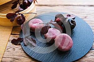 a black plate topped with purple balls and leaves on a wooden table.Mochi asian dessert