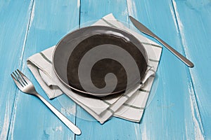 Black Plate with utensils and dish towel on blue wooden background with perspective