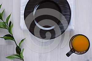 Black plate on white wooden background. With plant and napkin,top view. Empty plate for serving with orange juice