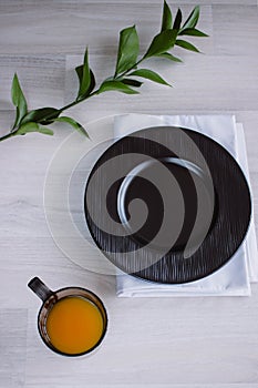 Black plate on white wooden background. With plant and napkin,top view. Empty plate for serving with orange juice