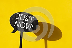 The black plate with written word JUST NOW isolated on yellow background photo