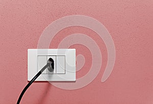 Black Plug in a Wall Socket on a Red Wall