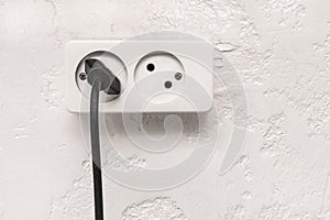 Black plug in white double socket on white plaster modern interior wall background