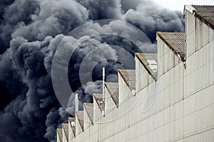 Black plumes of smoke from an accidental toxic industrial fire as seen from a behind a factory building.