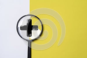 Black plus sign inside of magnifier glass on yellow and white background for focus positive thinking mindset of personal