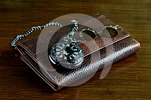 Black Pocket Watch with Leather Wallet and Gold Cuff Links on a Wooden Table Top