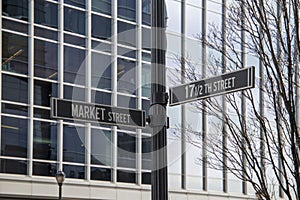 A black pole with street signs on Market Street and 17 Â½th Street with bare winter trees and buildings at Atlantic Station in photo
