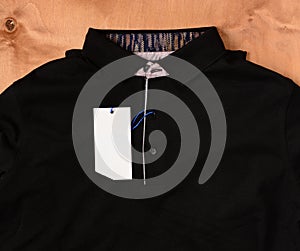 Black polo shirt with white tag on a wooden background