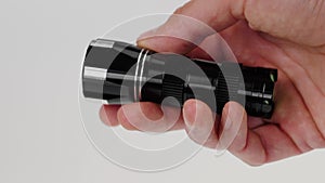 Black portable flashlight in hand. Turn on by pressing the start button with finger.