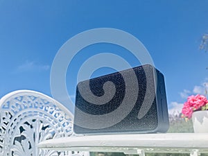 Black portable speaker on white garden table under blue sky.