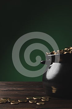 Black pot of golden coins on wooden table on green