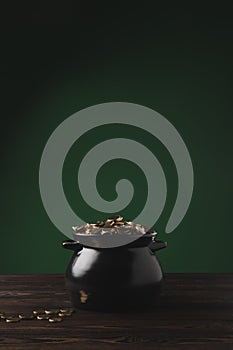 Black pot of golden coins on wooden table on green