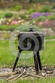 Black pot on high legs stands in the garden.