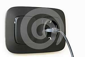 Black power cord cable plugged into european wall outlet on whit
