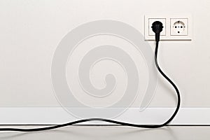 Black power cord cable plugged into european wall outlet on whit