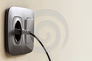 Black power cord cable plugged into european wall outlet on whit