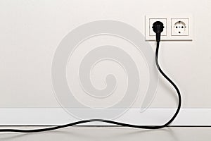 Black power cord cable plugged into european wall outlet on whit photo