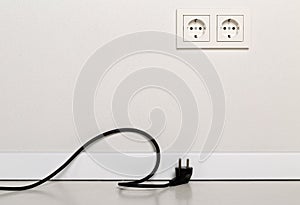 Black power cord cable unplugged with european wall outlet on white plaster wall