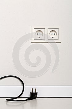 Black power cord cable unplugged with european wall outlet on white plaster wall