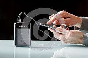 Black powerbank with a black cord charging  smartphone in a male hands on a black