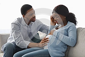 Black pregnant lady feeling sick, worried husband sitting by her