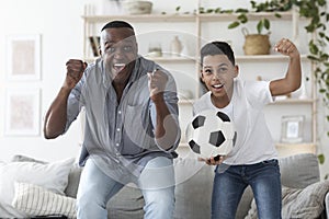 Black preteen boy watching football match on tv with his grandad