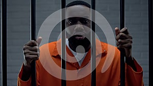 Black prisoner holding bars and looking at camera, drug dealer punishment