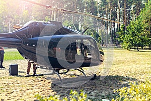 Black private modern luxury helicopter standing on grass field near forest at country rural landscape. Rich buiness lifestyle