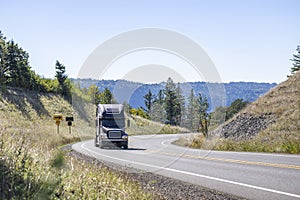 Black pro big rig semi truck transporting cargo in semi trailer climbing uphill on the winding mountain narrow road in Columbia