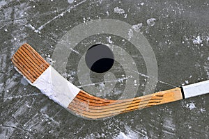 Black puck and hockey stick lying on a ice rink.