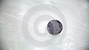 Black puck rotates on ice of ice hockey stadium. Slow motion