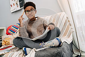 Black puzzled boy doing homework while sitting on sofa